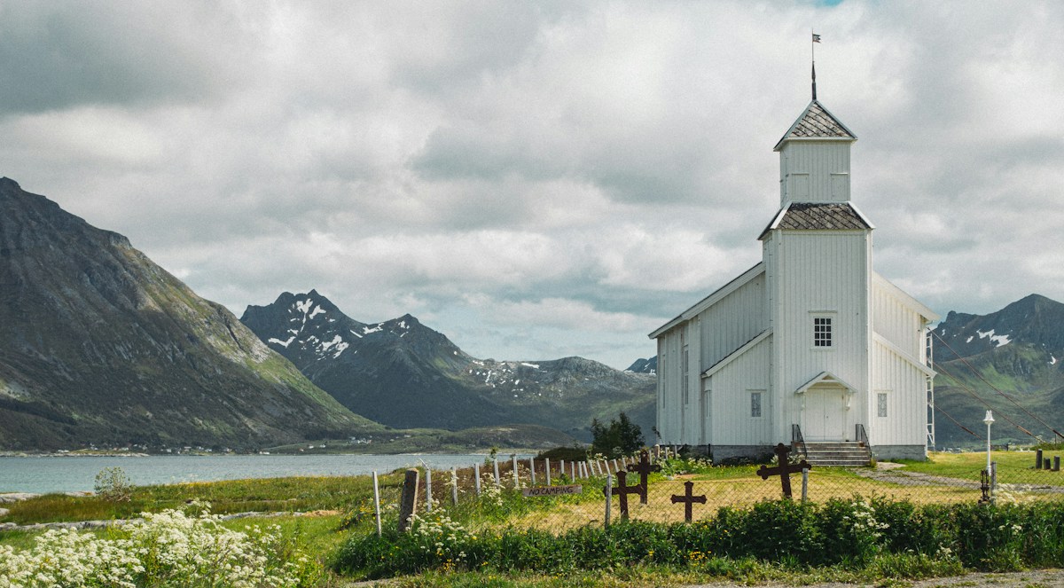 A white church with a steeple on a grassy hill