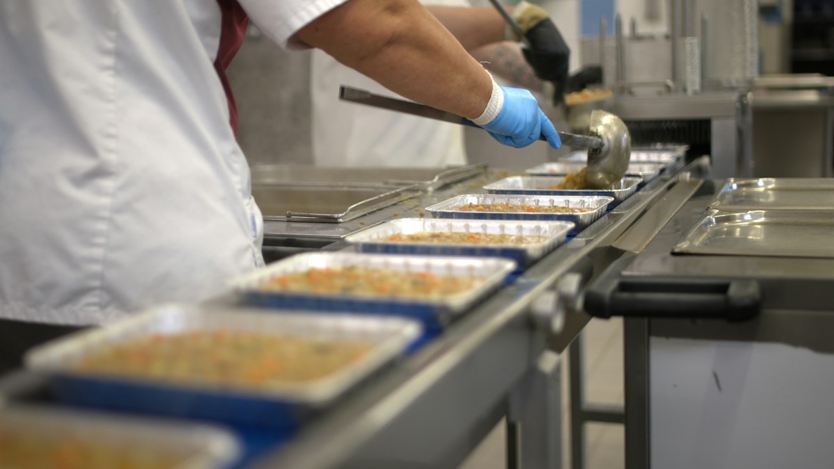 Worker filling food trays on a conveyor belt in a food processing plant