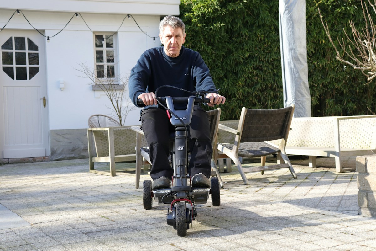 Man riding a three-wheel mobility scooter on a patio