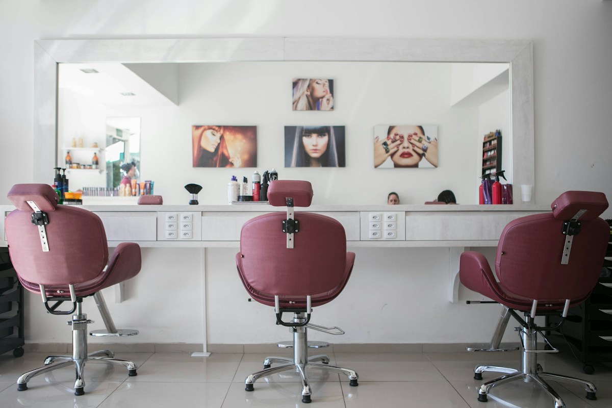 Hair salon chairs facing a long counter with a large mirror