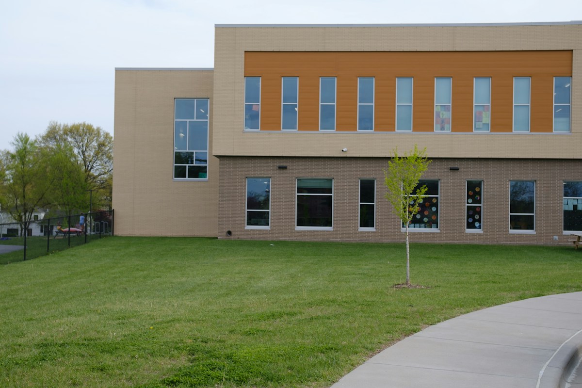 A modern school building with tan brick walls and a green lawn