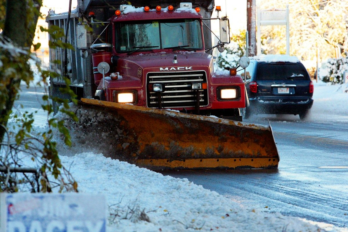 A snow plow driving down a snow covered road