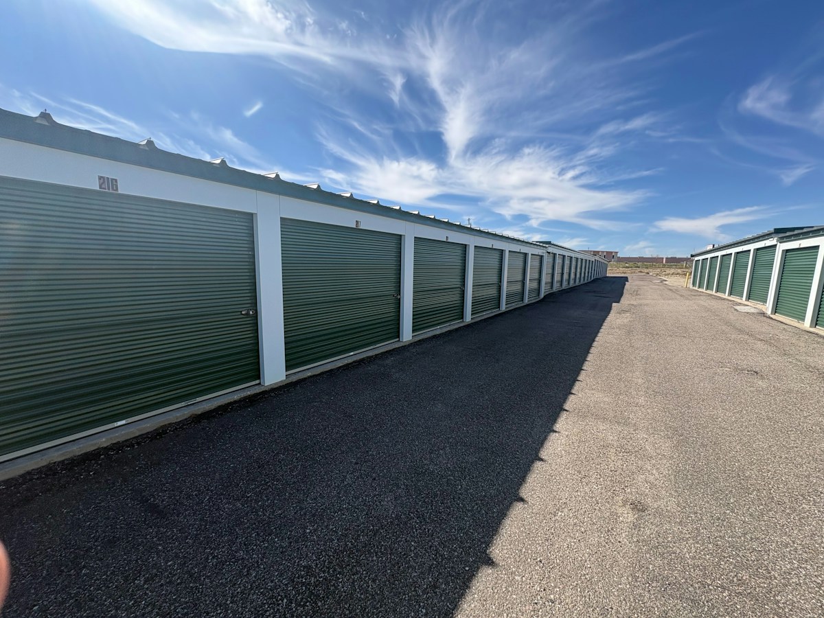 Rows of self-storage units with green metal doors under a blue sky